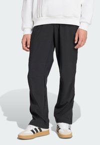 Svarta lätta byxor med avslappnad passform, med veck, sidofickor och texturerade detaljer, kombinerat med vita sneakers och en vit sweatshirt.