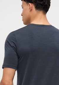 T-shirt grigio a maniche corte con collo rotondo, texture liscia e leggero lucido. Dettagli delle cuciture visibili sulle spalle e sulla schiena.