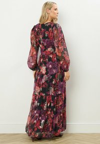 Maxiklänning i genomskinlig svart tyg med blommönster i djup röd och lila, med långa puffärmar och en lagerpåverkad design.