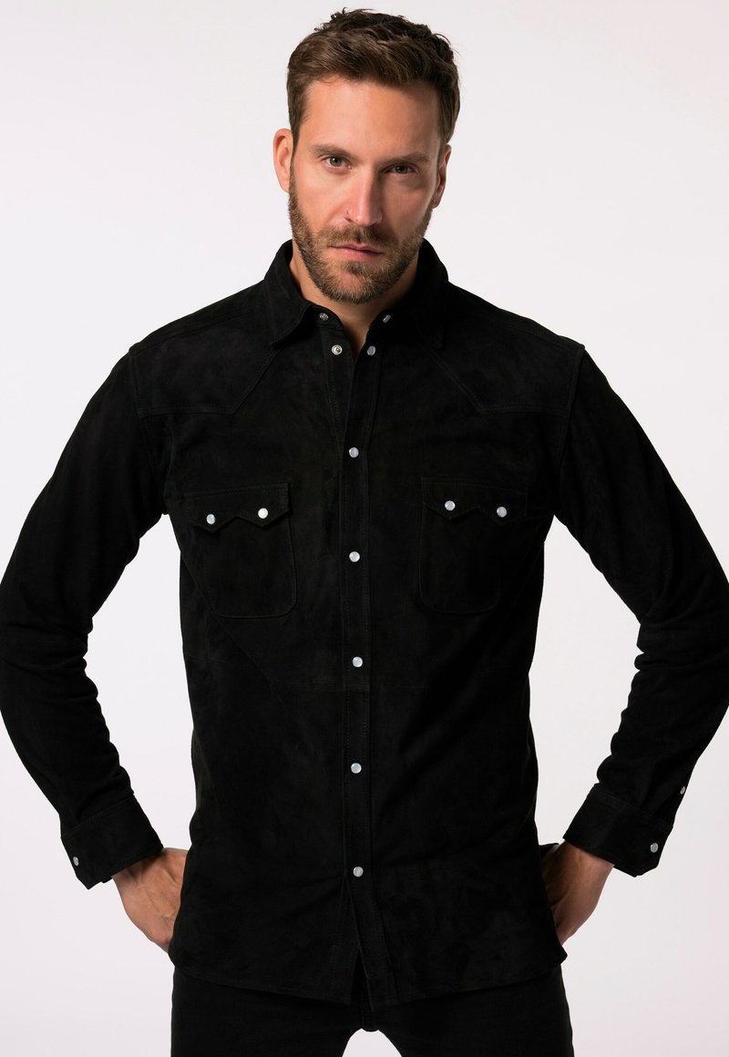 Camicia in suede nera con colletto a punta, bottoni a pressione, due tasche sul petto con pattina e maniche lunghe. Texture liscia in tutta la sua estensione.