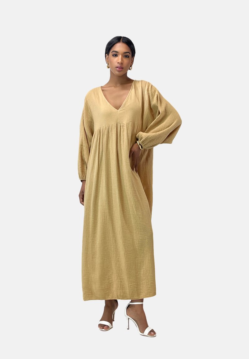 Robe longue et surdimensionnée en tissu texturé de couleur jaune clair avec un décolleté en V et des manches bouffantes, accompagnée de sandales à talons hauts blanches.