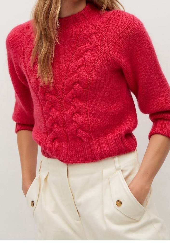 Femme portant un pull en maille torsadée rouge vif à manches bouffantes et un pantalon crème taille haute avec poches latérales à boutons.