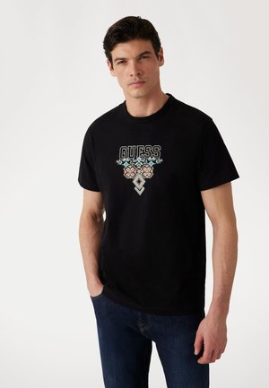 Tricou negru din bumbac cu logo-ul brodat "GUESS" în mai multe culori și modele geometrice, guler rotund și mâneci scurte.