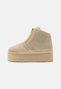 Stivali ankle in suede beige con punta arrotondata, suola piatta e zip laterale. Presentano dettagli cuciti lungo le cuciture.