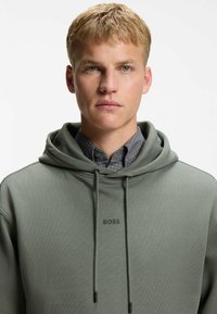 Green hoodie with a textured finish, featuring an adjustable drawstring and the brand name "BOSS" embroidered in dark green on the chest.