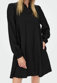 Czarna sukienka z długim rękawem, z zapięciem na guziki przy kołnierzy, w luźnym kroju i z marszczonymi mankietami. Miękka tkanina o gładkiej fakturze i lekko rozkloszowanym fasonie.