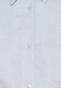 Chemise boutonnée bleu clair en lin avec une finition texturée, dotée d'un col et de deux poches avant, agrémentée de boutons blancs.