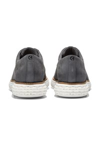 Zapatos de cuero gris con detalles perforados, una suela media texturizada blanca y acentos marrones. El diseño presenta una forma redondeada y un talón acolchado.