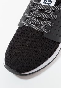 Czarne sneakersy z siateczkową cholewką, szarymi sznurówkami i białą podeszwą środkową. Posiada perforowane akcenty oraz zaokrąglony design nosa.