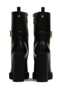 Black leather ankle boots with gold hardware, block heels, side zippers, and matching straps. Textured surfaces add detail and depth.
