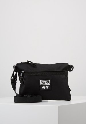 Czarna torebka na ramię z przednią kieszenią na suwak i regulowanym paskiem, z kwadratową naszywką z logo "OBEY".
