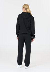 Felpa nera con cappuccio e pantaloni abbinati, realizzati in tessuto morbido; presenta una vestibilità comoda e polsini elastici sulle maniche e sulle caviglie.