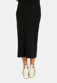 Czarna spódnica midi w wzory z falbaniastym dołem, połączona z białymi butami na słupku z dekoracyjnymi akcentami i wycięciami.