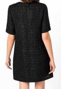 Robe noire à manches courtes avec un tissu texturé et tissé présentant un éclat subtil. Coupe droite avec une fermeture éclair au dos.