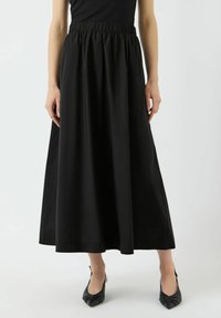 Jupe noire longueur cheville avec taille élastiquée, tissu lisse et silhouette ample. Associée à des talons noirs à bouts pointus.