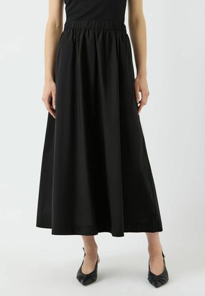 Falda negra hasta el tobillo con cintura elástica, tela lisa y silueta completa. Combinada con zapatos de tacón negros y punta puntiaguda.