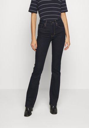 Dark blue denim jeans with a flared design, high waist, five pockets, and contrasting orange stitching. Paired with a striped short-sleeve top.