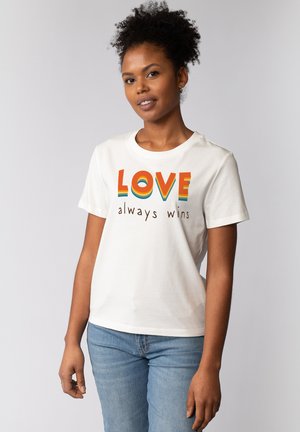 Witte katoenen t-shirt met bold, meerkleurige tekst die "LOVE" in regenboogstrepen en "always wins" in bruin weergeeft. Korte mouwen, ronde hals.