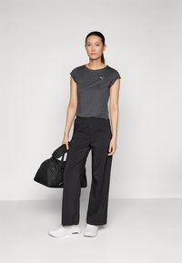 Camiseta atlética gris de manga corta, pantalones de pierna ancha negros, zapatillas blancas y una bolsa de deporte negra. Diseño simple y funcional.