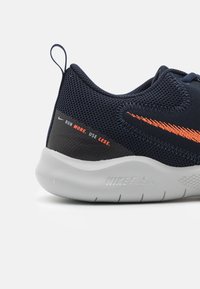 Chaussure de course Nike avec une tige en mesh bleu marine et une bande d'accent orange, un col rembourré et une semelle intermédiaire en caoutchouc grise avec des détails texturés.