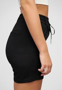 Svarte stretchshorts med elastisk midjebånd, drakksnøring og sidelommer. Glatt tekstur og tilpasset passform.