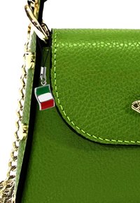 Groene leren handtas met gouden hardware, een textuur oppervlak en een decoratieve Italiaanse vlag charm, bevestigd met een zwart koord.