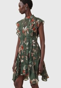 Green floral dress with ruffled short sleeves, pleated front detailing, and uneven hemline; made of lightweight, textured material.