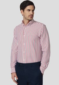 Czerwona i biała w paski koszula na guziki z długimi rękawami i spiczastym kołnierzykiem, wykonana z gładkiego materiału i dopasowanym kroju.
