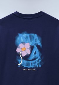 Μπλε-σκούρο μπλουζάκι με μπλε και μωβ γραφικό κείμενο, με στυλιζαρισμένο ροζ λουλούδι και λευκό κοτσάνι. Κάτω από το σχέδιο, είναι γραμμένο το "Κάνε τη Σημάδα σου" με λευκά γράμματα.