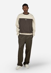 Pánská dvoubarevná fleecová mikina v krémové a tmavě hnědé barvě, s kulatým výstřihem a malým logem. Spárována s odpovídajícími tmavě zelenými kalhotami.