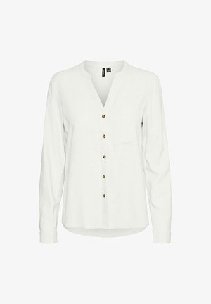 Camisa blanca de manga larga con escote en V, que presenta una fila de botones marrones en la parte frontal y un bolsillo en el pecho. Tejido suave y texturizado.