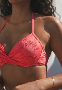 Corall rózsaszín, háromszögletű bikini felső, textúrált virágmintával és vékony pántokkal, dekoratív arany kiegészítővel.