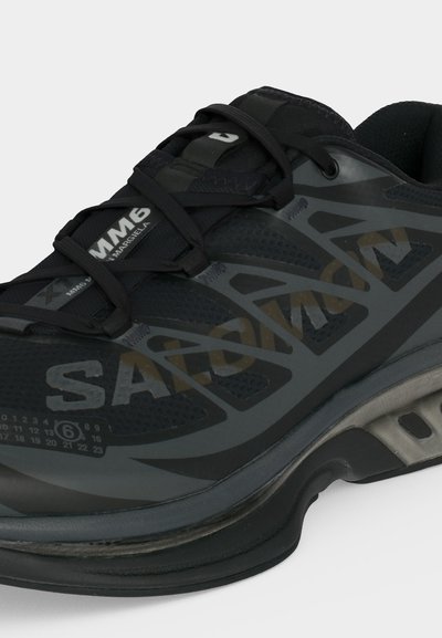 Μαύρο αθλητικό παπούτσι με διαπνέον ύφασμα και συνθετικές επικαλύψεις, παχιά σόλα με ορατή απορρόφηση κραδασμών και με λογότυπο στη πλευρά και τη γλώσσα.