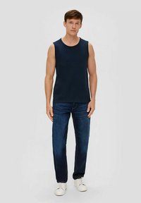 Marineblaue ärmellose Shirt aus Baumwolle, runder Ausschnitt, kombiniert mit dunkelblauen Jeans und weißen Turnschuhen.