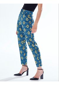 Blue patterned trousers with diamond shapes in yellow. Fitted design, ankle length, made from a smooth fabric. Worn with black heels.