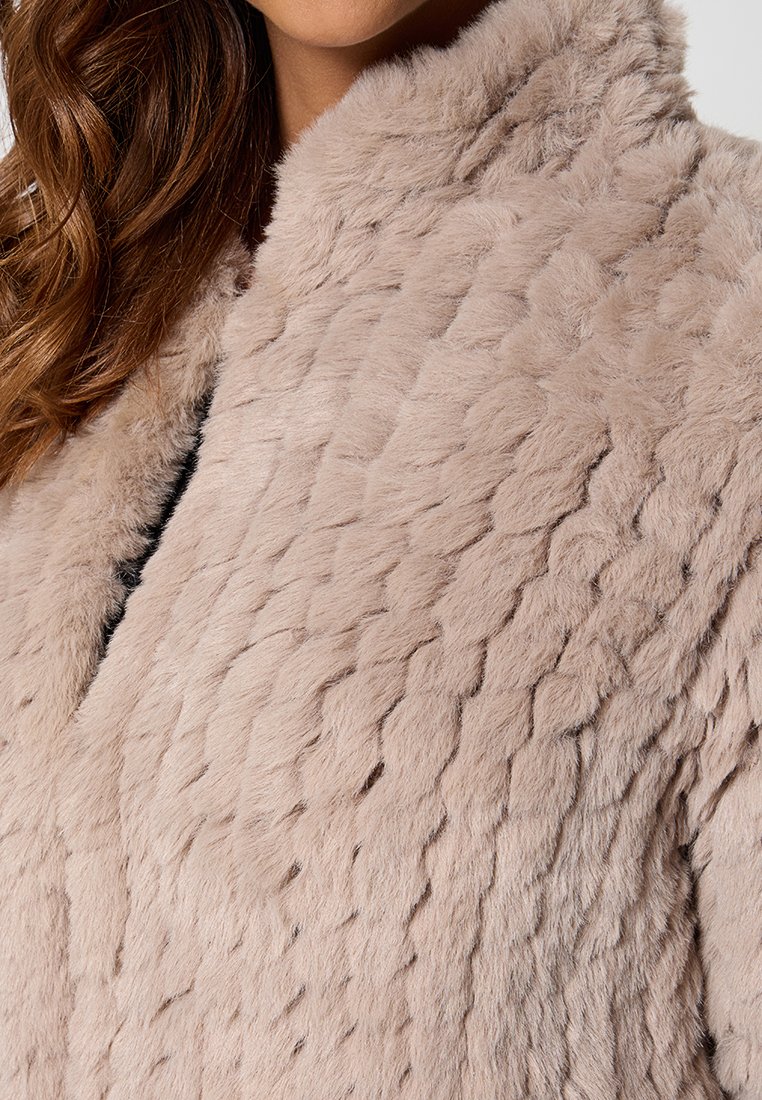 Kołnierzowy płaszcz z sztucznego futra w odcieniu różowego bluszu, z teksturowanym falistym wzorem, miękką powierzchnią i kołnierzem mandarynki. Brak widocznych zapięć lub zdobień.
