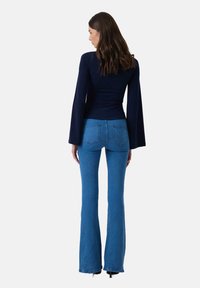 Navy long-sleeve top with flared sleeves paired with high-waisted blue jeans featuring a classic five-pocket design and slight distressing.