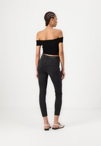 Μαύρη μπλούζα χωρίς ώμους σε συνδυασμό με σκουρό�χρωμο γκρι κολάν. Το σύνολο διαθέτει μινιμαλιστικό σχέδιο και διακριτή ραφή, συμπληρωμένο από ανοιχτόχρωμες σανδάλια.