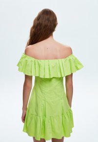 Vestido off-the-shoulder en un vibrante verde lima, con un escote con volantes y un dobladillo con volantes en capas, hecho de una tela ligera.