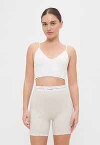 Baltas trumpas viršus su plonomis petnešėlėmis, derinamas su šviesiai pilkais raibuotais šortais su balta elastinga juosta, ant kurios yra "Calvin Klein" logotipas.