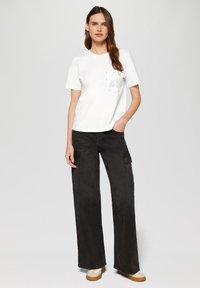 Witte katoenen t-shirt met korte mouwen en een zak met een bloemontwerp. Gecombineerd met losse zwarte cargobroeken en beige schoenen.