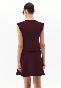 Burgunderfarbener Strick-Zweiteiler mit einem kurzen Top und einem ausgestellt geschnittenen Rock. Sanfte Textur, kurze Ärmel und taillierter Schnitt. Minimalistisches Design.