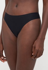 Schwarzer Bikiniunterteil aus glattem Stoff, mit einem hochgeschnittenen Design und minimaler Bedeckung. Schlichte und nahtlose Kanten für besonderen Komfort.