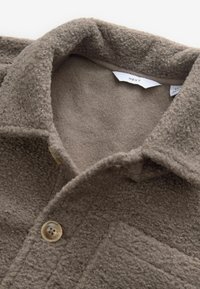 Cămașă din fleece, cu nasturi, de culoare maronie deschisă, cu un guler texturat, având un model ușor matlasat și un închidere cu un singur nasture.