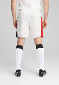 Hvide shorts med grå grafisk mønster, rød sidepanel, sorte accenter; båret med sorte støvler og knæhøje hvide sokker med teksturerede striber.