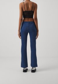 Pantalons évasés bleus avec une finition texturée et étincelante, et une ceinture élastique. Portés avec un crop top en dentelle noir et des chaussures à plateforme.