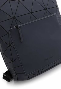 Jūrinis geometrinis kuprinė, pagaminta iš sklandžios sintetinės medžiagos, turi akcentuotą užtrauktuko kišenę ir tekstūruotą trikampį raštą.