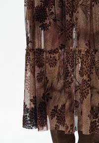 Doorzichtige bruine jurk met bloemrijke borduursels in donkerrood en zwart. Heeft gelaagde ruches en een gestructureerde afwerking over het geheel.