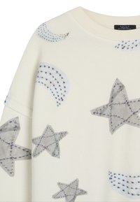 Felpa crema con design di stelle grigie e lune crescenti, cuciture multicolori, tessuto testurizzato e vestibilità rilassata.