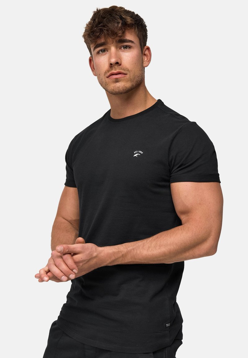 Camiseta de algodón negra con cuello redondo, mangas cortas y un logo blanco en la parte superior del pecho izquierdo. Textura suave y corte clásico.